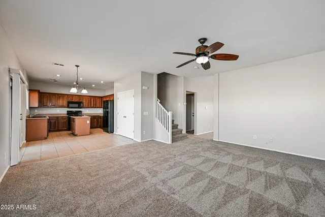 a living room with kitchen and a chandelier fan