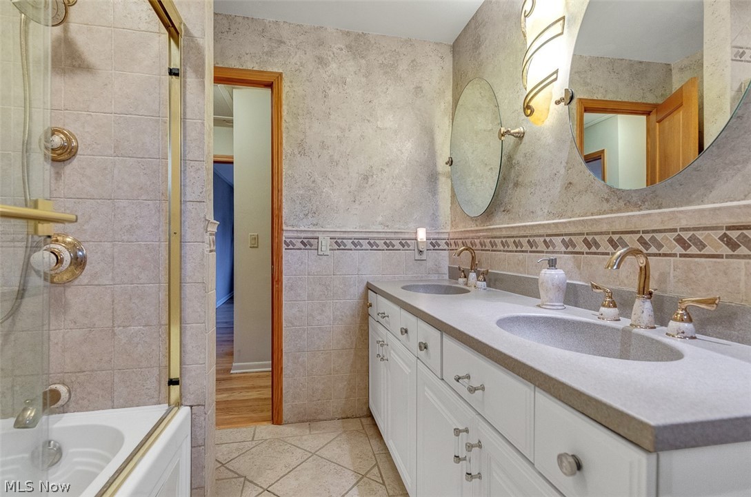 2990 Hampton Road Cleveland, OH 44120 - Photo 23 of 29 Full bath with double vanity, tiled shower / bath, light tile patterned floors, tile walls, and a wainscoted wall