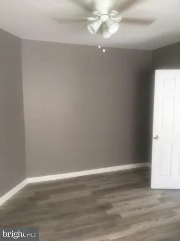 a view of an empty room with wooden floor and fan