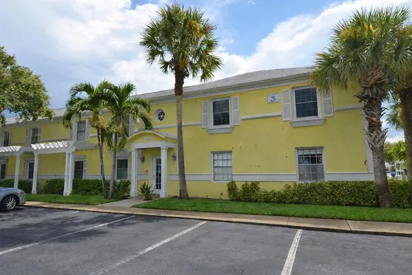 a view of a white house with a large windows and a lawn chair and palm trees