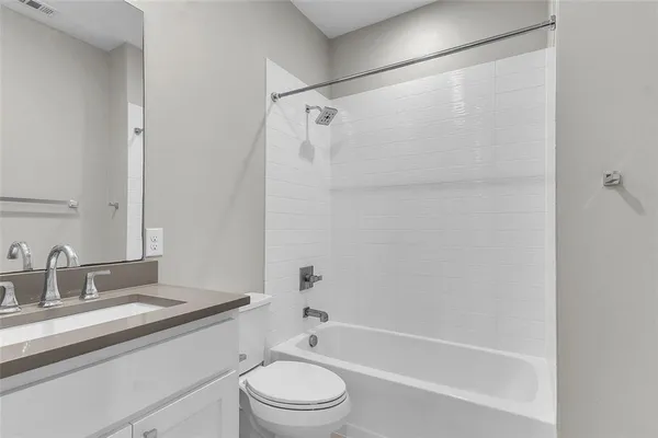 a bathroom with a granite countertop bathtub shower sink vanity and toilet