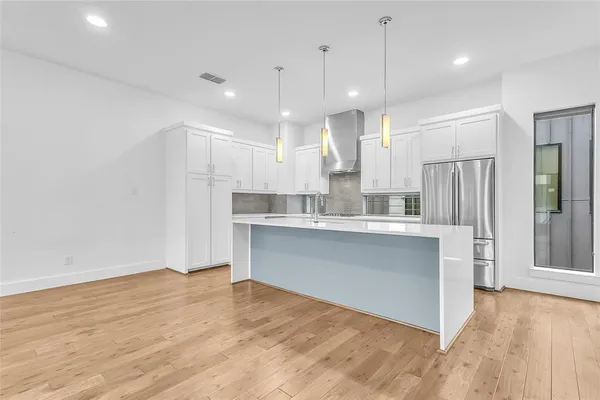 a large white kitchen with a refrigerator a sink dishwasher a stove and white cabinets with wooden floor