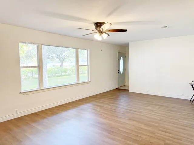 an empty room with wooden floor fan and windows