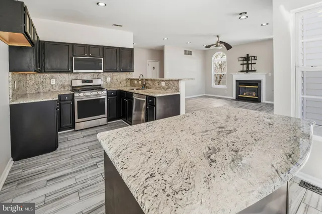 a kitchen with stainless steel appliances kitchen island granite countertop a stove top oven a sink and dishwasher with wooden floor