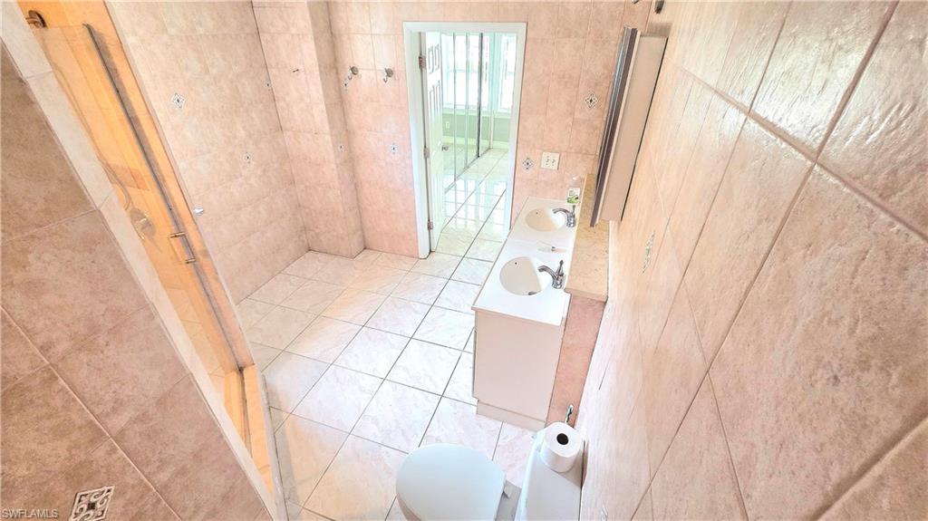 5529 Hardee Street Naples, FL 34113 - Photo 9 of 17 Tile flooring throughout featuring a dual vanity with undermount sinks, a toilet, and a glass-enclosed shower