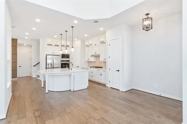 a large white kitchen with a stove a sink dishwasher and a refrigerator with wooden floor