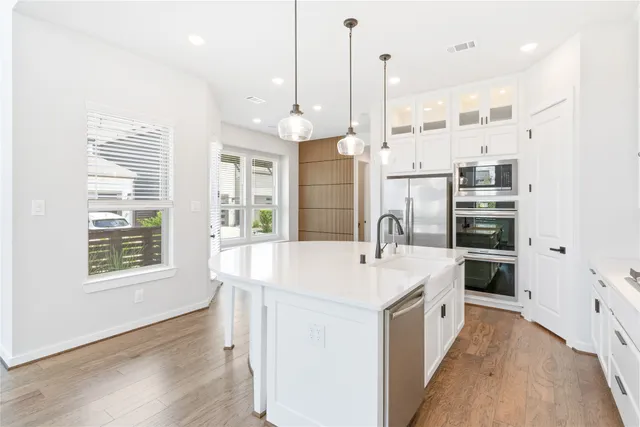 a large white kitchen with a stove a sink a kitchen island with a countertop cabinets and a wooden floor