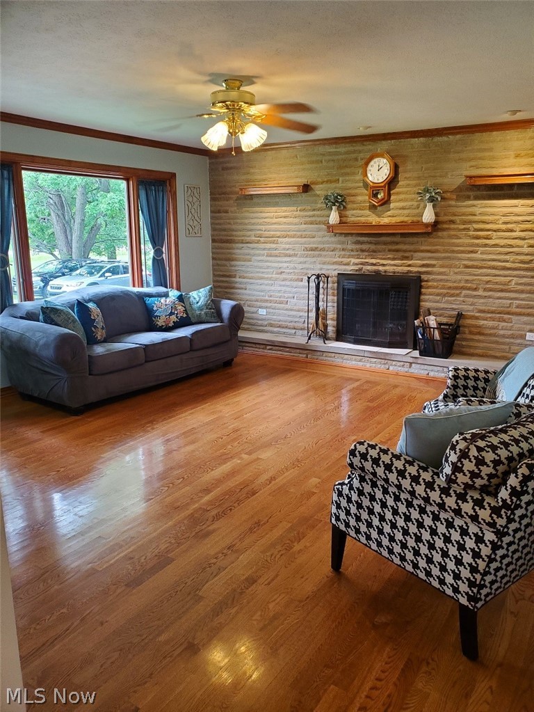 1284 Substation Road Brunswick, OH 44212 - Photo 8 of 26 Living room featuring a fireplace, ornamental molding, wooden walls, wood-type flooring, and ceiling fan
