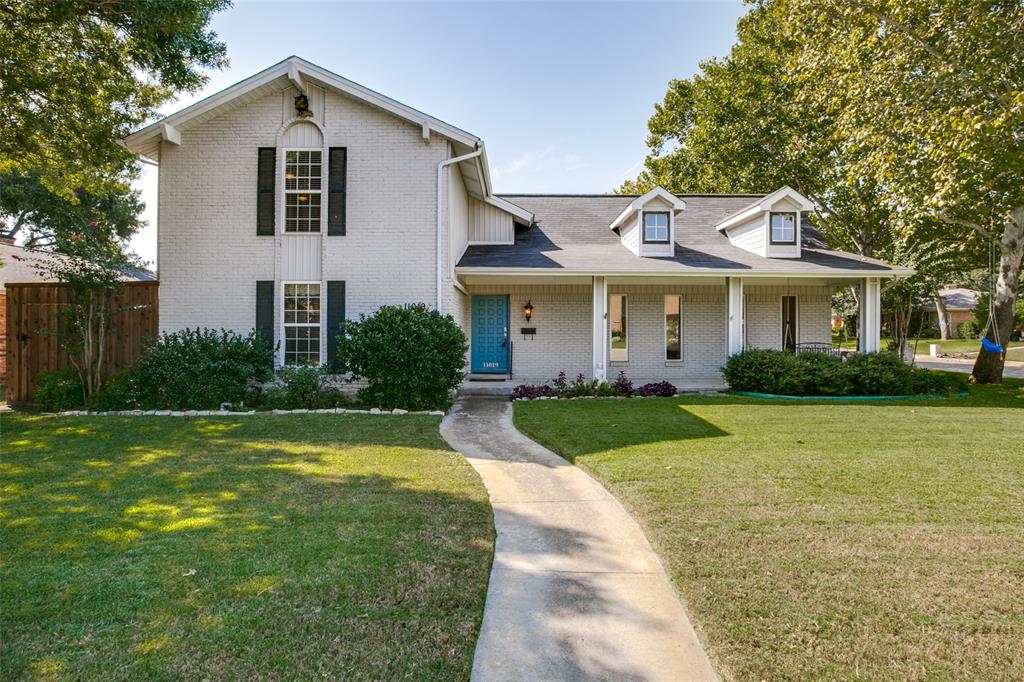a view of a white house with a yard plants and a large tree