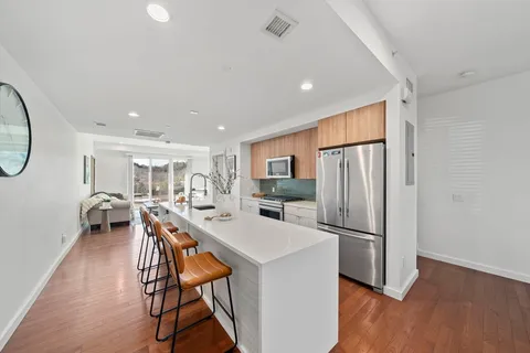 a kitchen with stainless steel appliances a refrigerator a stove a dining table and chairs with wooden floor