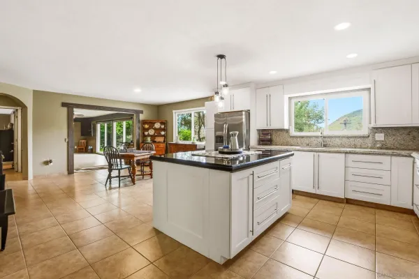 a kitchen with stainless steel appliances granite countertop a stove top oven a sink a dining table and chairs with white cabinets