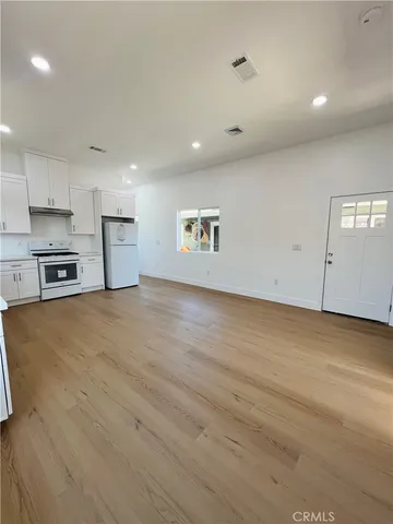 an empty room with kitchen view and a refrigerator