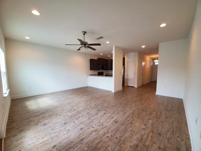 an empty room with wooden floor and a kitchen