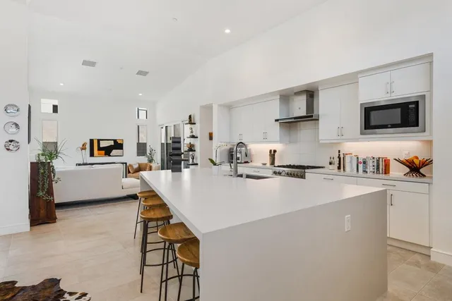 a living room with stainless steel appliances kitchen island granite countertop a sink a stove and a refrigerator with wooden floor