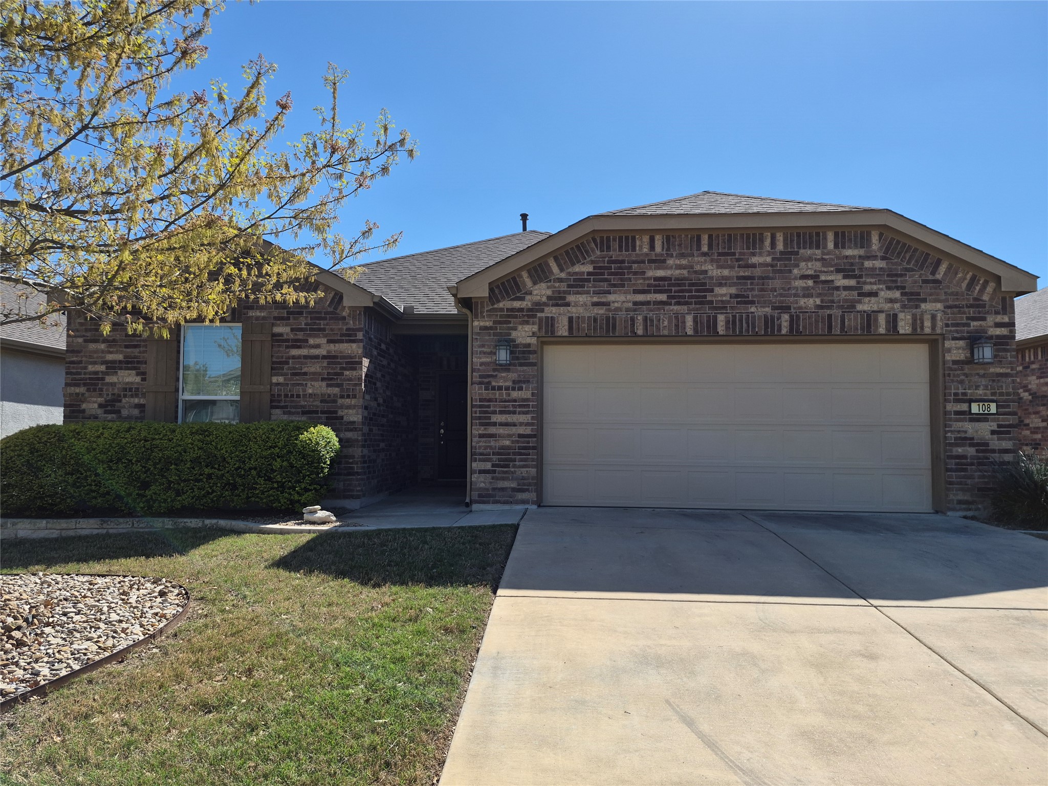 Ranch-style house featuring brick siding, driveway, an attached garage, a front yard, and a shingled roof