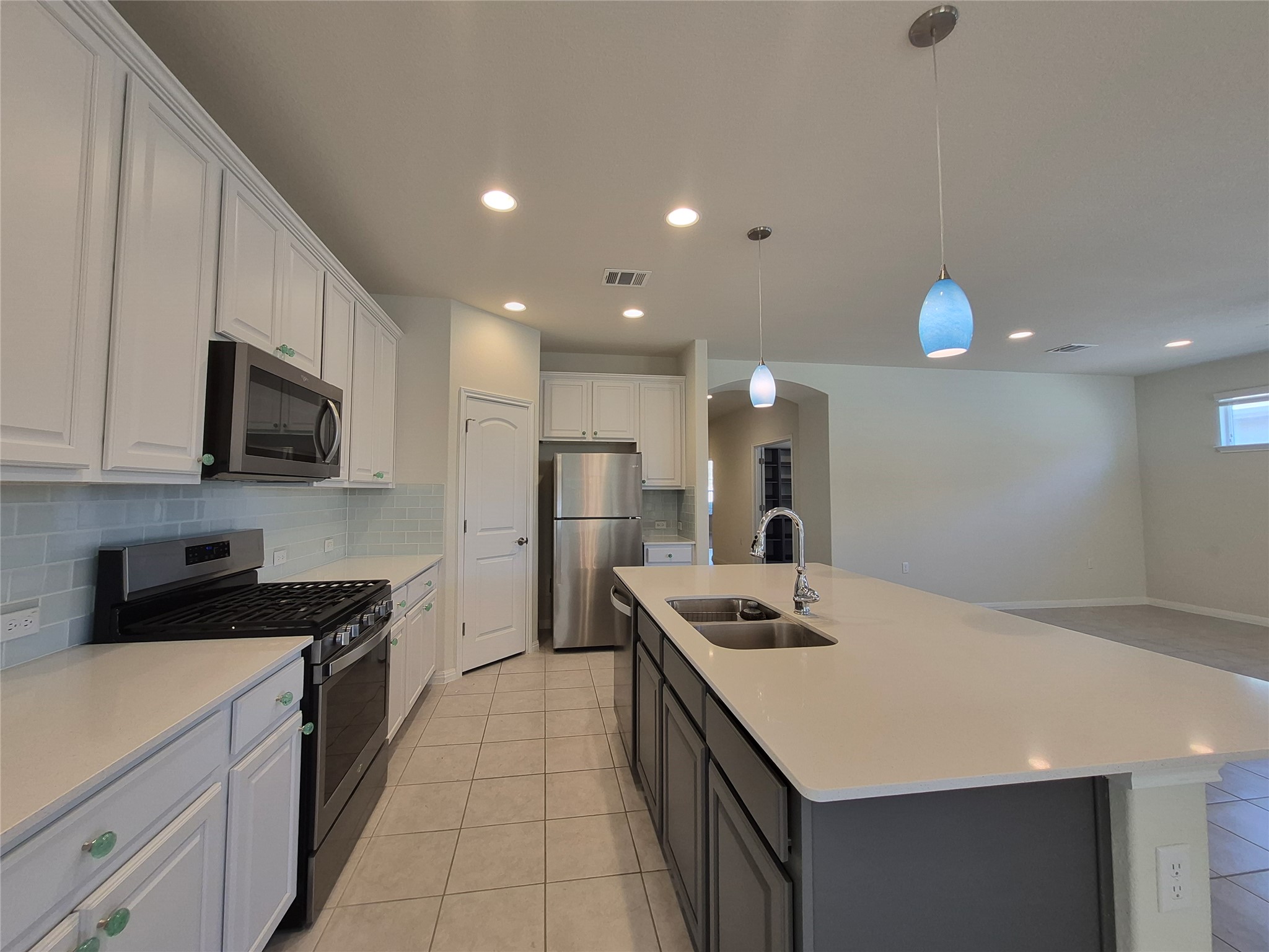 108 Calhoun Lane Georgetown, TX 78633 - Photo 9 of 27 Dual tone kitchen with stainless steel appliances, an island with sink, decorative light fixtures, backsplash, and light stone counters