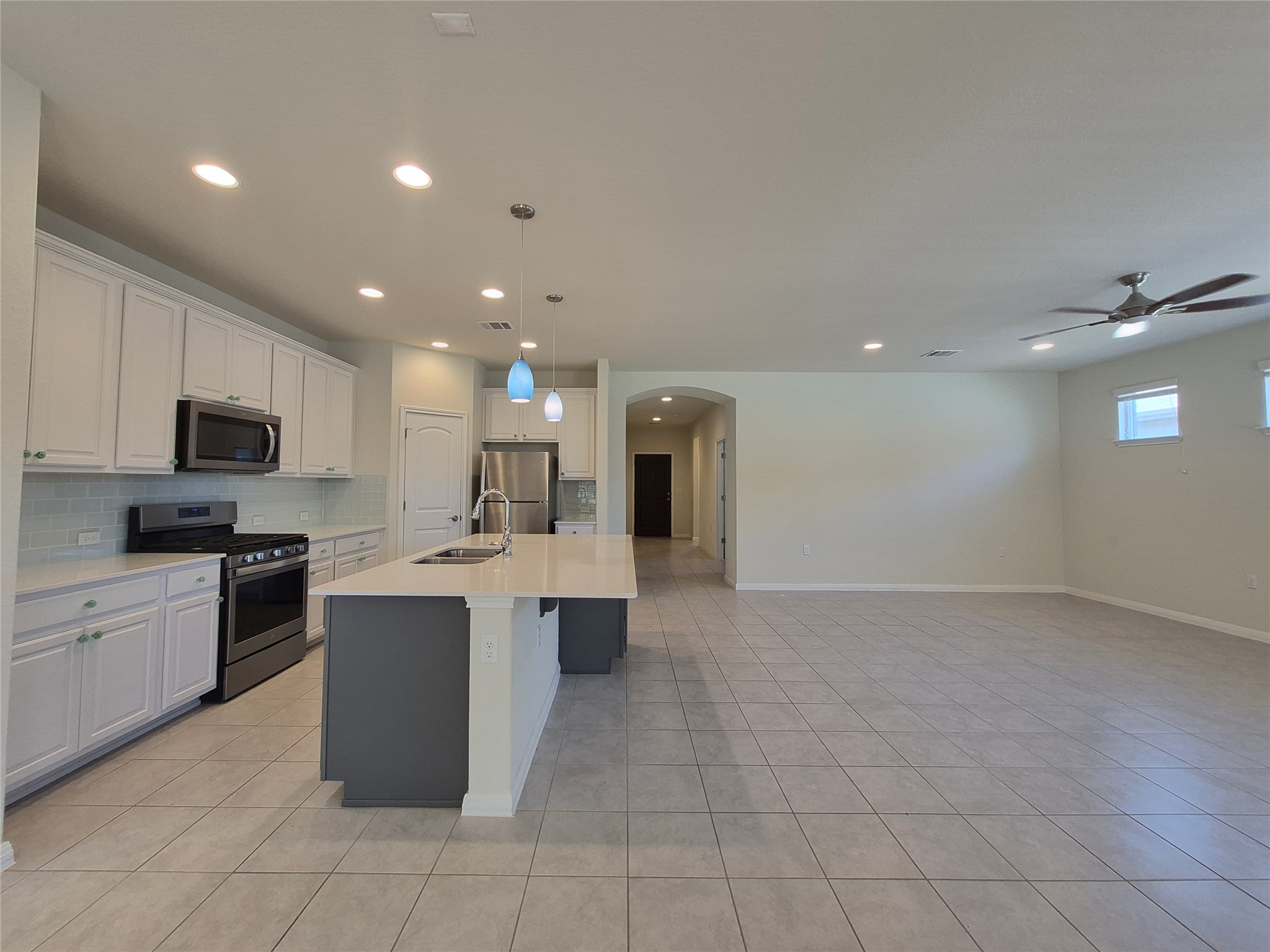 108 Calhoun Lane Georgetown, TX 78633 - Photo 4 of 27 Dual tone kitchen with arched walkways, stainless steel appliances, an island with sink, hanging light fixtures, and ceiling fan