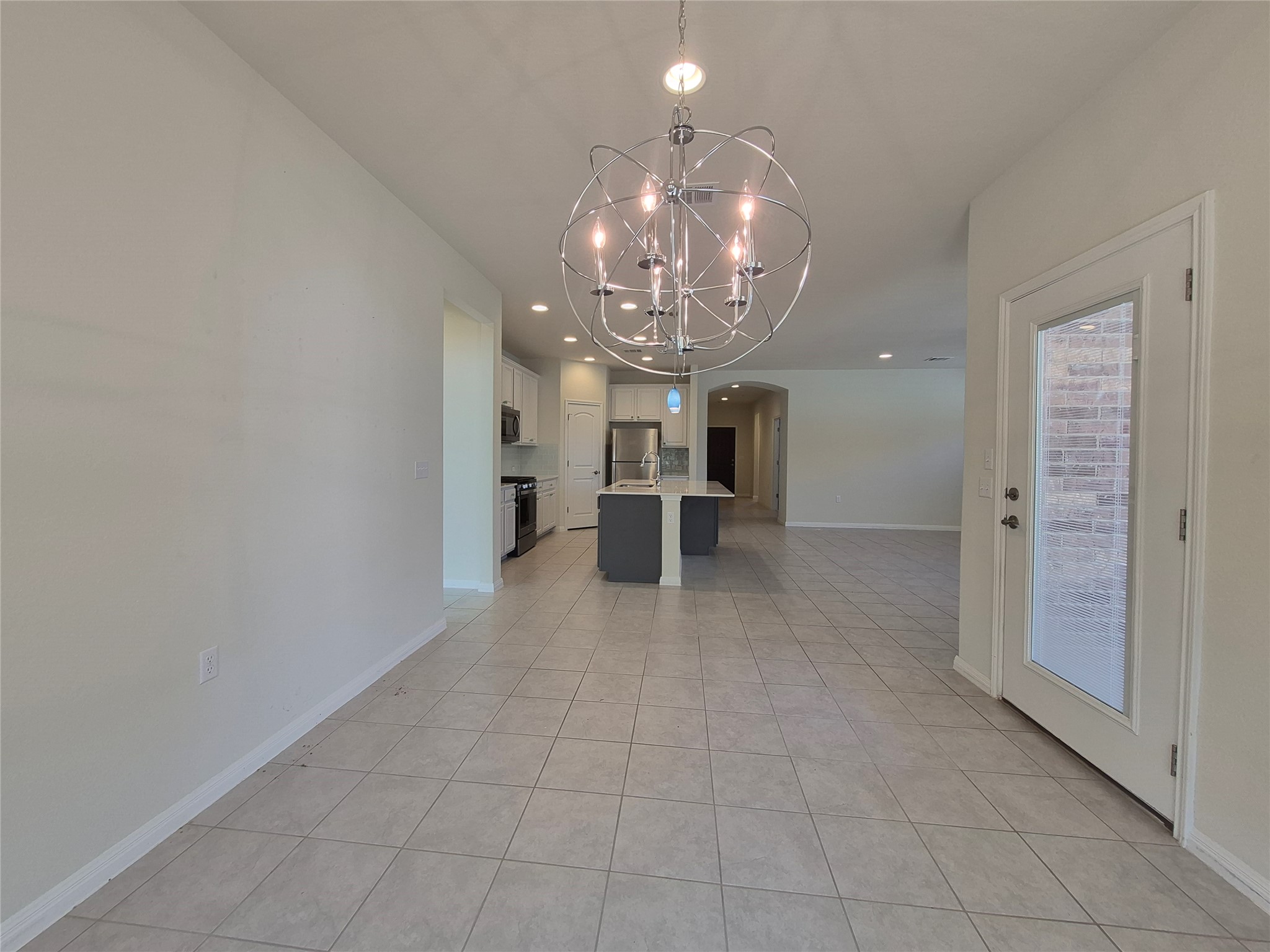 108 Calhoun Lane Georgetown, TX 78633 - Photo 5 of 27 Kitchen featuring an island with sink, arched walkways, suspended lighting, stainless steel appliances, and light tile patterned floors