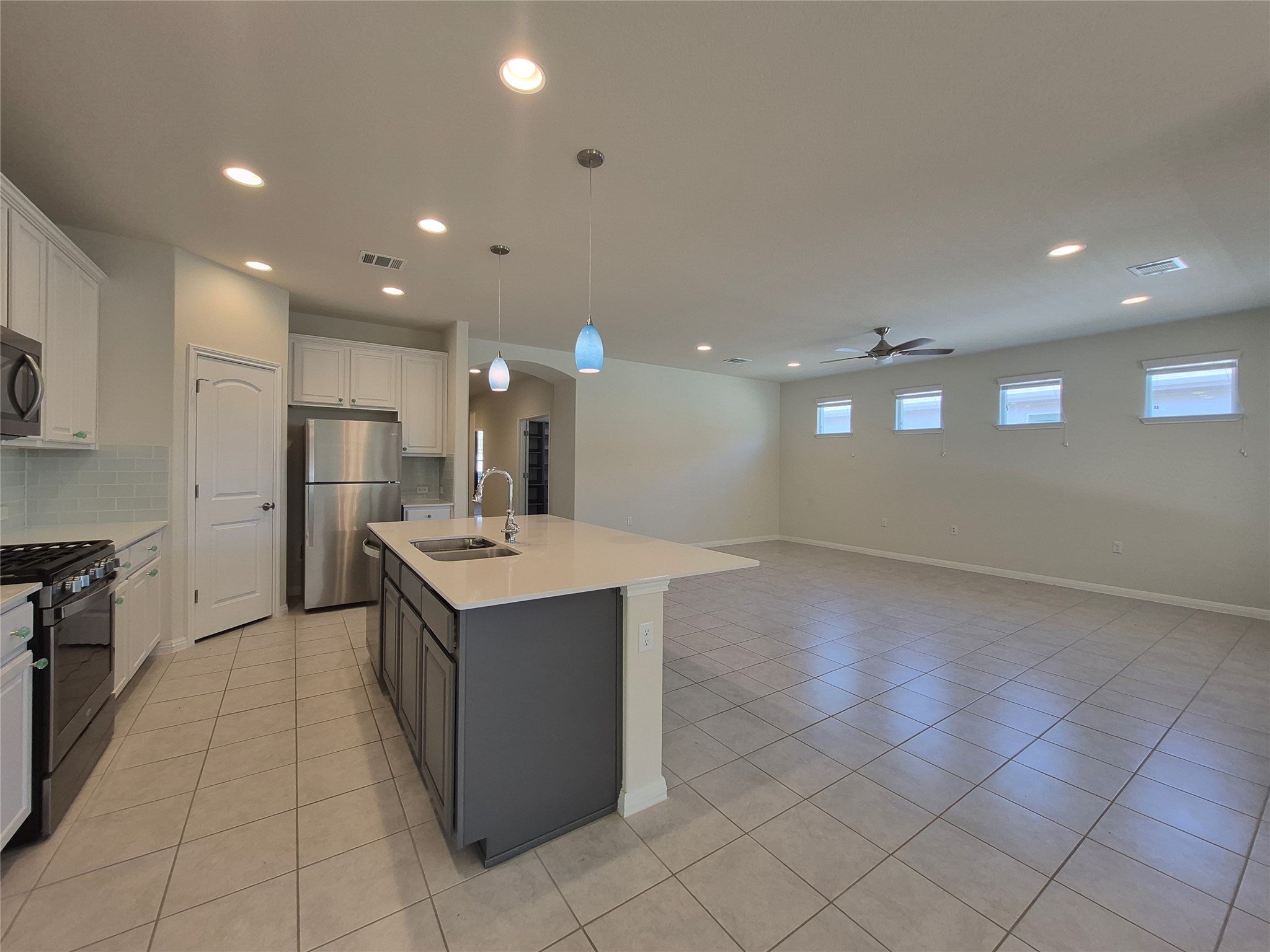 108 Calhoun Lane Georgetown, TX 78633 - Photo 8 of 27 Two tone kitchen featuring stainless steel appliances, arched walkways, dual tone cabinetry, an island with sink, and decorative light fixtures