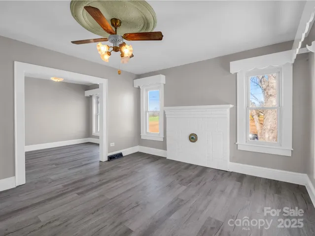 an empty room with wooden floor chandelier fan and windows