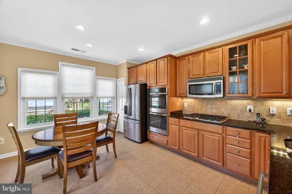 a kitchen with stainless steel appliances granite countertop a stove top oven a refrigerator a sink and a dining table with chairs