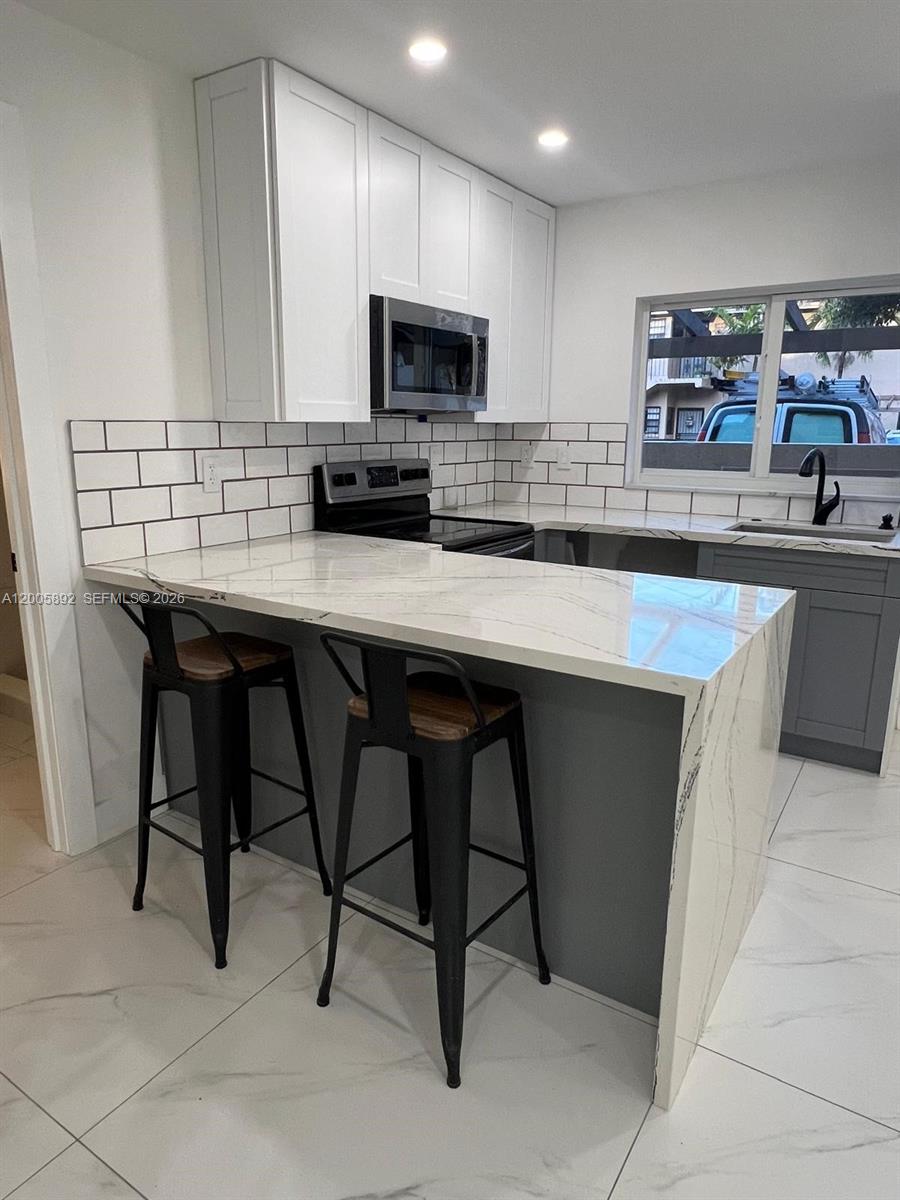 3632 Southwest 112th Avenue, Unit 63 Miami, FL 33165 - Photo 8 of 14 a kitchen with stainless steel appliances kitchen island granite countertop a table chairs microwave and sink