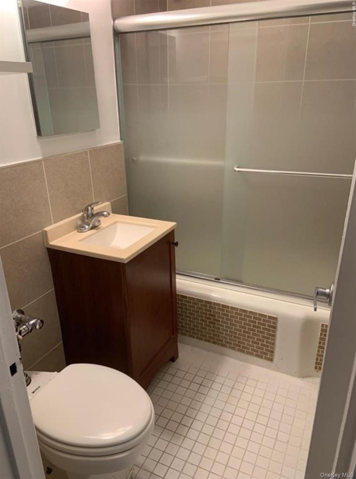 34-10 75th Street, Unit 3L Queens, NY 11372 - Photo 9 of 18 Bathroom featuring an enclosed shower, tile walls, vanity, toilet, and tile patterned floors