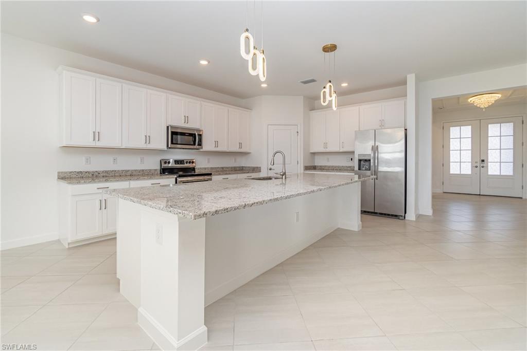 11127 Canopy Loop Fort Myers, FL 33913 - Photo 4 of 29 Kitchen with stainless steel appliances, light stone countertops, white cabinets, a center island with sink, and light tile patterned floors