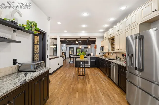 a kitchen with stainless steel appliances granite countertop a refrigerator a stove top oven a sink dishwasher and couches with wooden floor