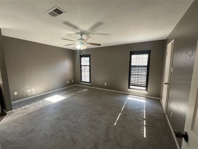 an empty room with chandelier fan and windows