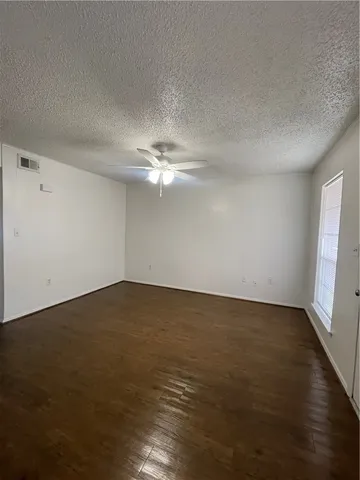 a view of an empty room with wooden floor and fan