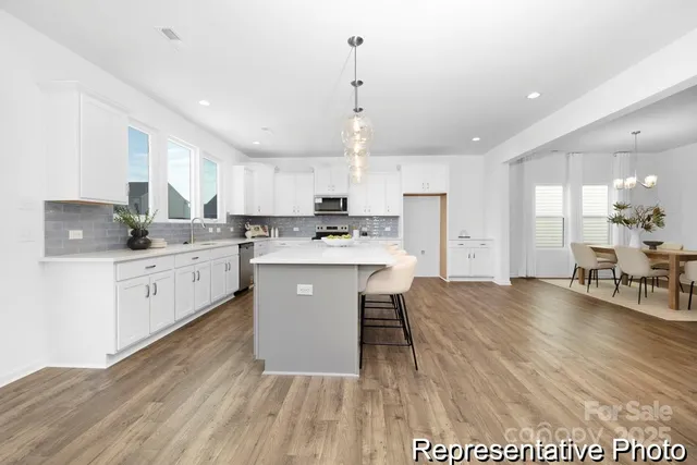 a kitchen with stainless steel appliances kitchen island granite countertop a stove a sink a refrigerator and white cabinets with wooden floor