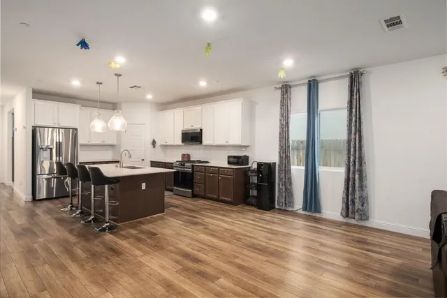 a kitchen with stainless steel appliances kitchen island granite countertop a refrigerator a sink dishwasher a stove and a refrigerator with wooden floor