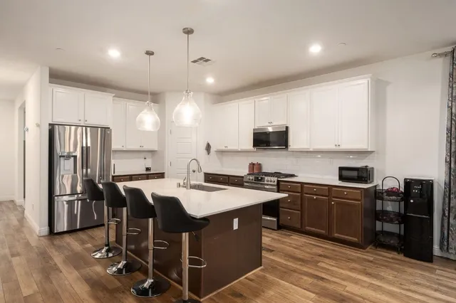 a kitchen with stainless steel appliances granite countertop a sink a stove a refrigerator and island with wooden floor