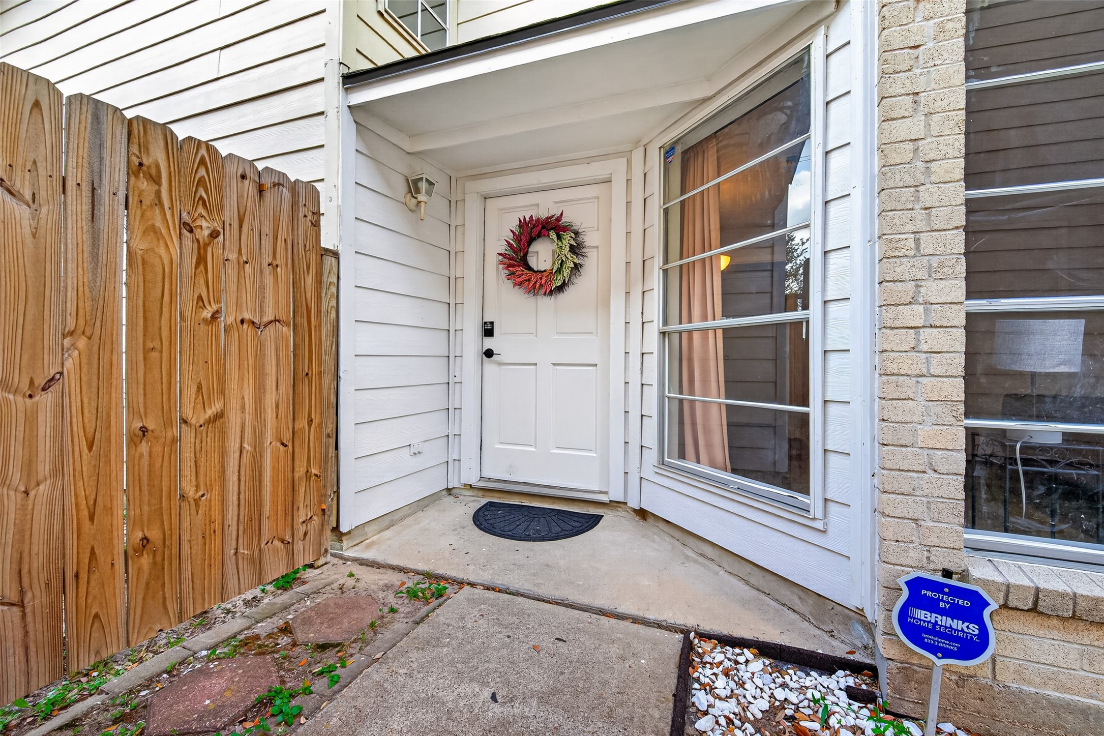 18446 North Willow Bluff Road Katy, TX 77449 - Photo 4 of 33 This photo shows a charming entryway with a white door adorned with a wreath. It features a cozy, covered porch area, large windows, and a wooden privacy fence. There's a security sign indicating a protected home.