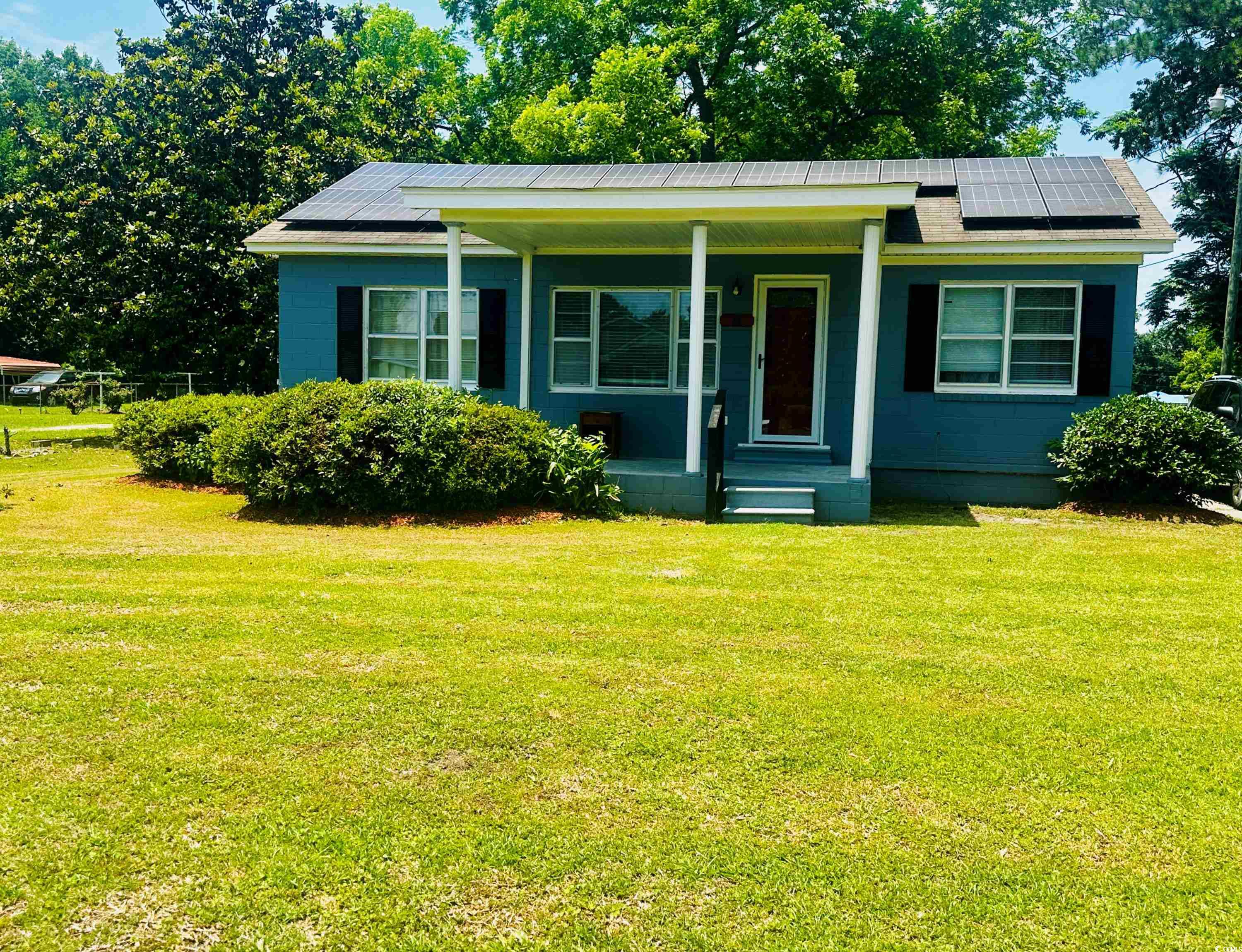 Bungalow-style house with solar panels, a front yard, a porch, and concrete block siding