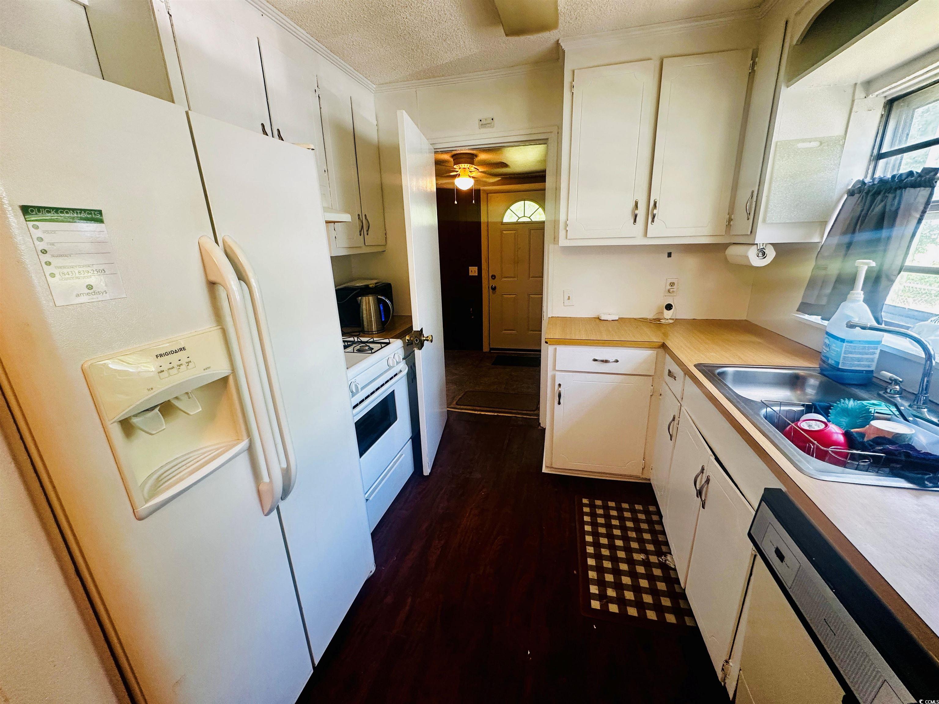 8 Raymond Street Andrews, SC 29510 - Photo 10 of 13 Kitchen featuring white appliances, light countertops, a textured ceiling, white cabinetry, and crown molding