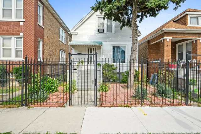 a view of a brick house with a large trees plants and wooden fence