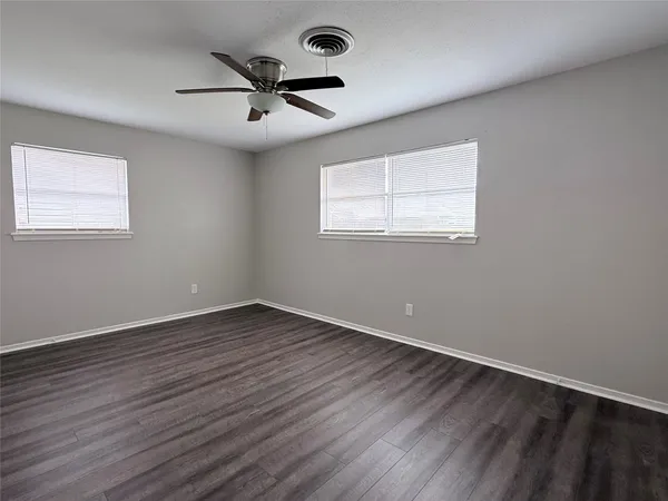 an empty room with wooden floor fan and windows