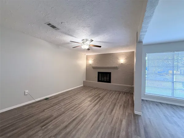 a view of an empty room with wooden floor fireplace and a window
