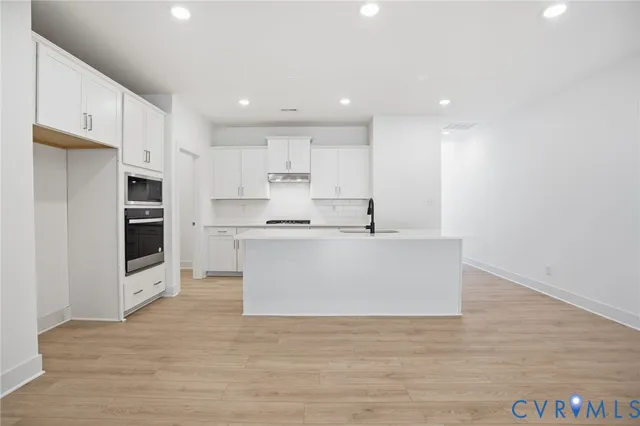a view of kitchen with kitchen island a sink white cabinets and stainless steel appliances