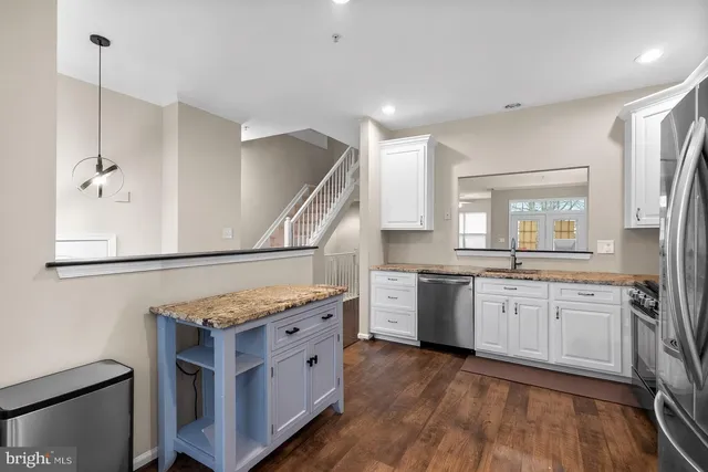 a kitchen with stainless steel appliances granite countertop a stove a sink dishwasher a refrigerator and white cabinets with wooden floor