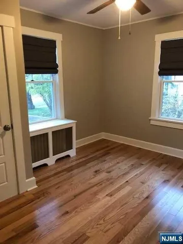 an empty room with wooden floor fan and windows