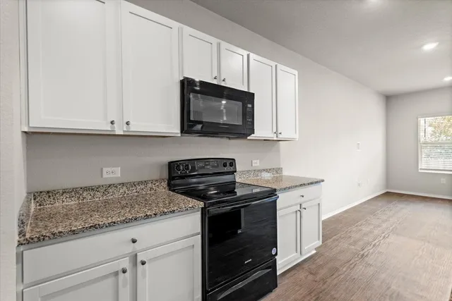 a kitchen with granite countertop white cabinets and a stove top oven
