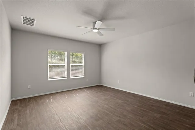 an empty room with wooden floor ceiling fan and windows