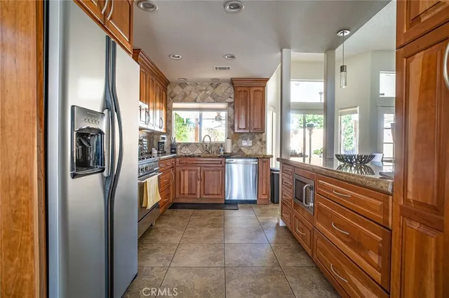 a kitchen with stainless steel appliances granite countertop a refrigerator a sink a stove and white cabinets with wooden floor