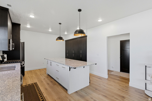 3902 West 825 North West Point, UT 84015 - Photo 21 of 49 Kitchen featuring light stone counters, a center island, light wood finished floors, a breakfast bar area, and pendant lighting