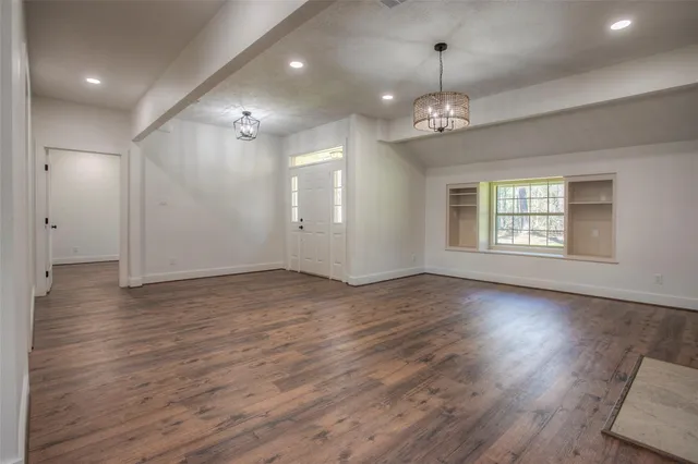 an empty room with wooden floor chandelier and windows