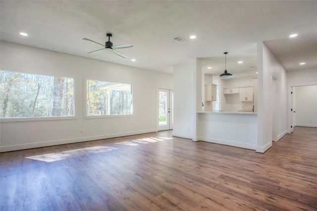 an empty room with wooden floor a ceiling fan and windows