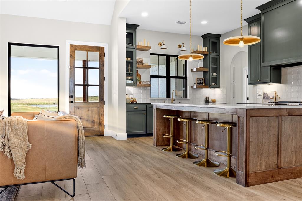 10978 Gregory Road Sanger, TX 76266 - Photo 13 of 40 Wood-finish flooring, dark green cabinetry, a central kitchen island with a light-toned countertop, and a glass-paneled wooden door